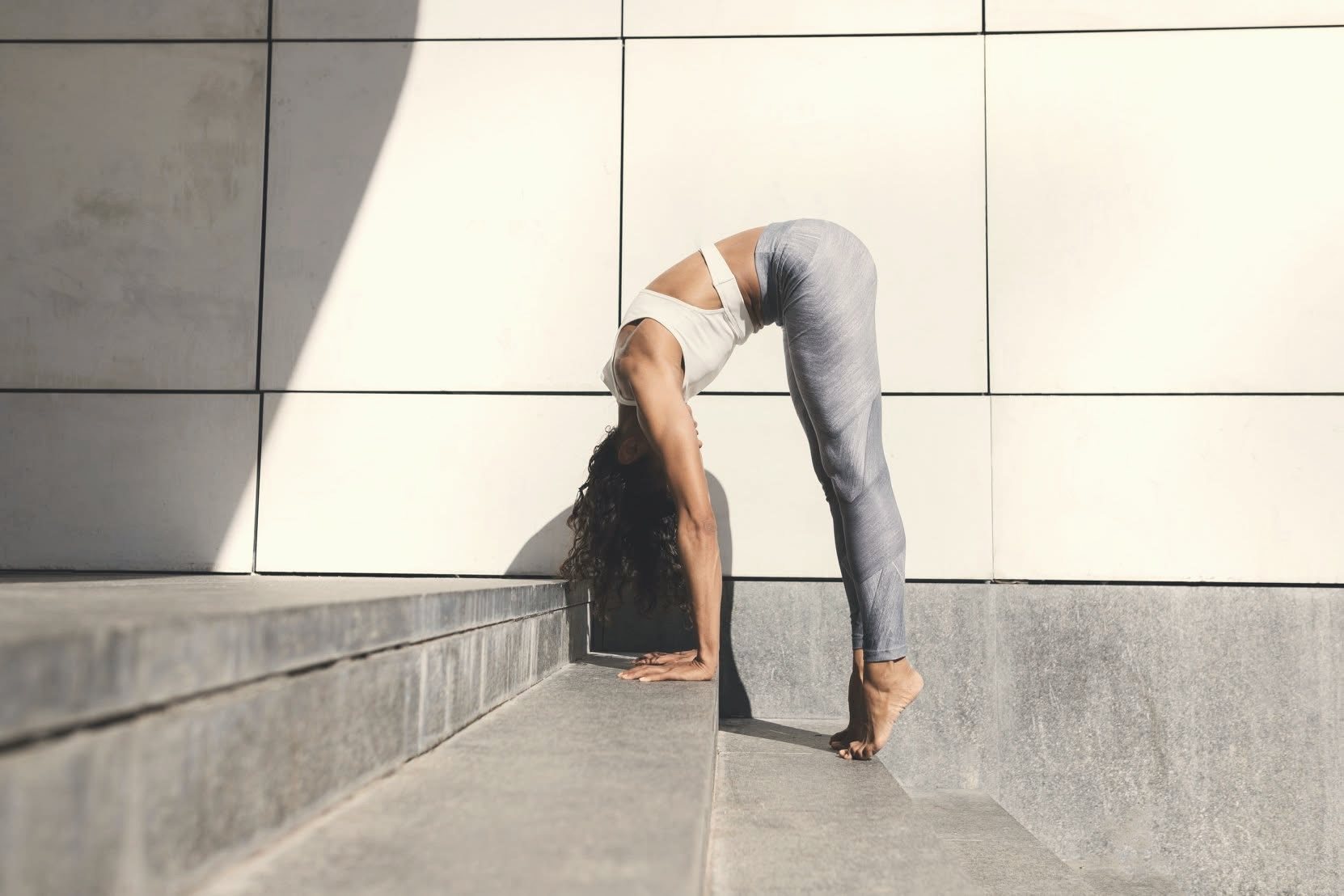 Practicante de yoga en una postura de pie junto a una pared iluminada por el sol